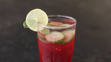 A tall glass with a red beverage, ice cubes, lime slice, and mint leaves.