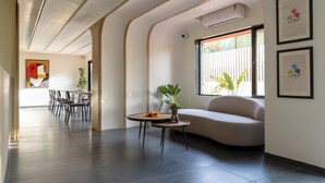 A modern living room with a sofa, a dining area with chairs, and a small table with a plant. - Saavi Suites (Daman)