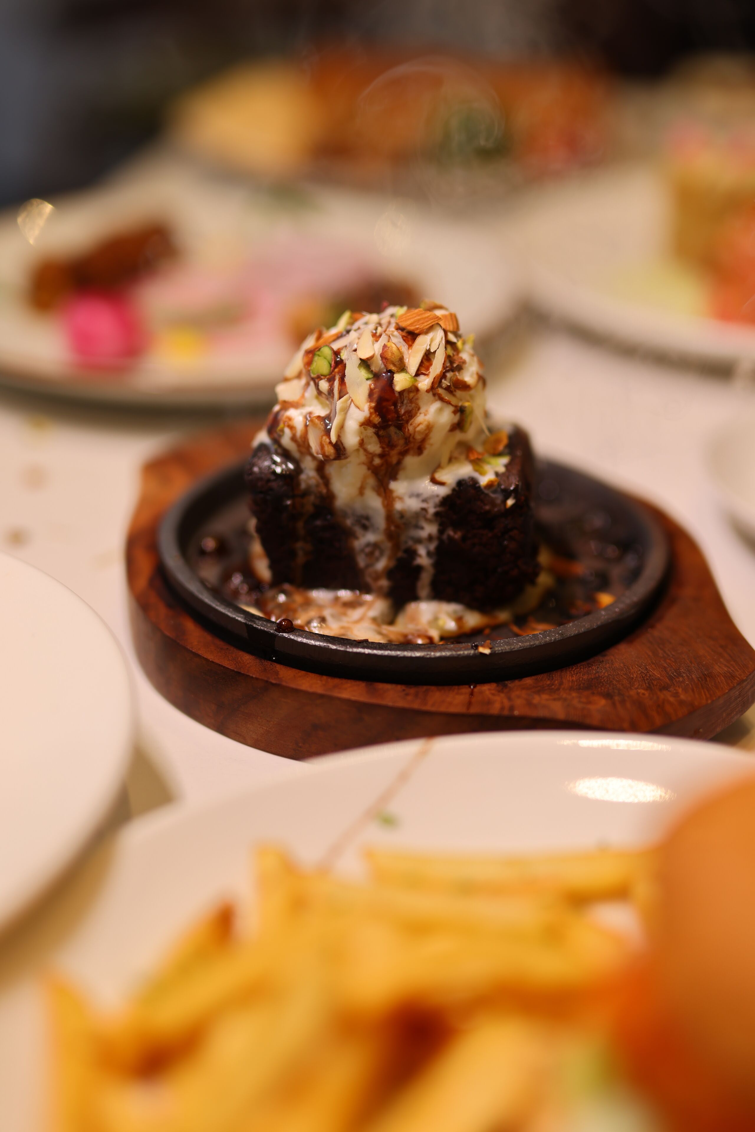 Un postre sobre un plato de madera con base oscura, cubierto de crema blanca y adornado con nueces.
