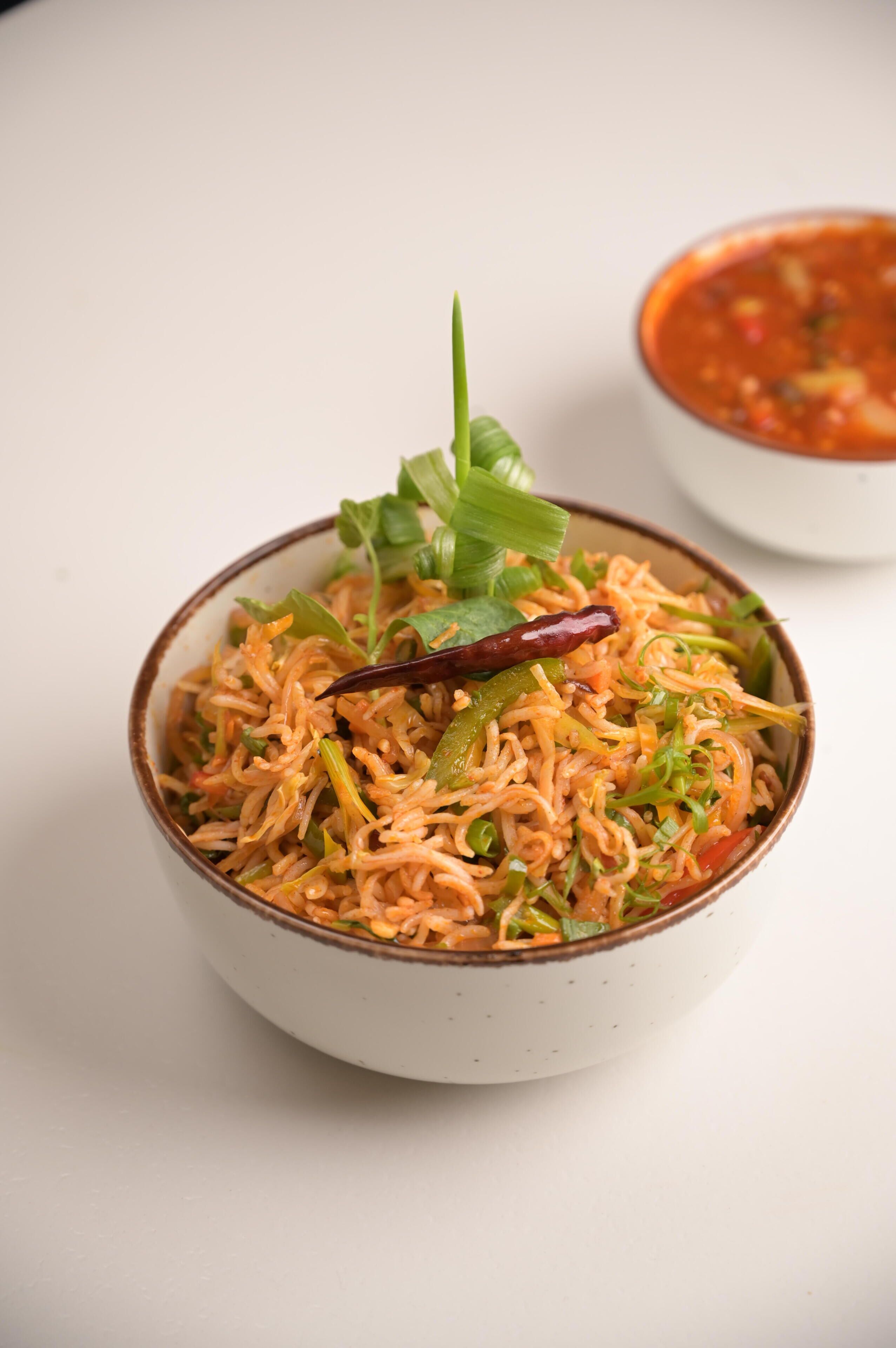 A bowl of food with a red chili and green garnish on top.