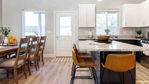 A modern kitchen with a central island, white cabinetry, and a dining area with wooden chairs.