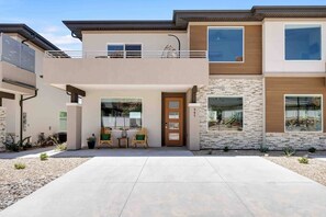 A modern two-story house with a balcony, a front door, and a small patio area with chairs and a table. - Grand Canyon-4bed,3bath,hot tub (Hildale)