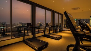 Une salle de sport équipée de tapis de course et d’appareils d’exercice, de grandes fenêtres offrant une vue sur la ville et un aménagement intérieur moderne.