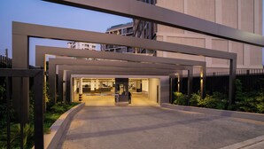 Une entrée moderne d’un bâtiment, avec une allée couverte, une personne qui marche et un bâtiment en arrière-plan.