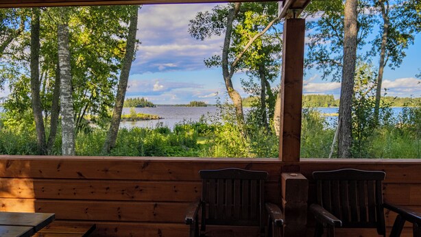 A wooden deck with two wooden chairs and a table, overlooking a lake and trees. - Holiday Village Anttoora - Anttooran Lomakylä (Pori)