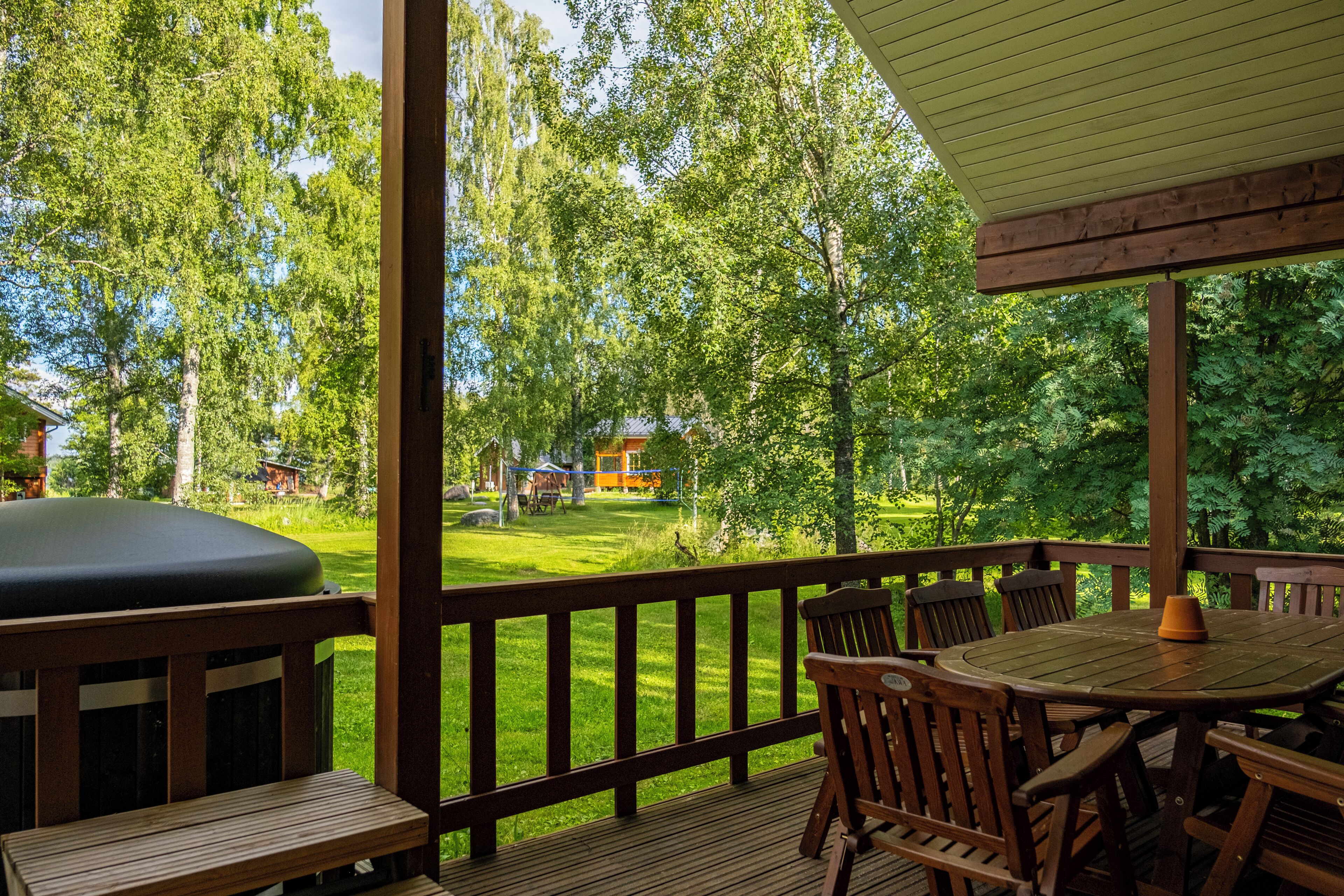 Eine Holzterrasse mit Tisch und Stühlen, mit Blick auf eine gepflegte Rasenfläche und Bäume.