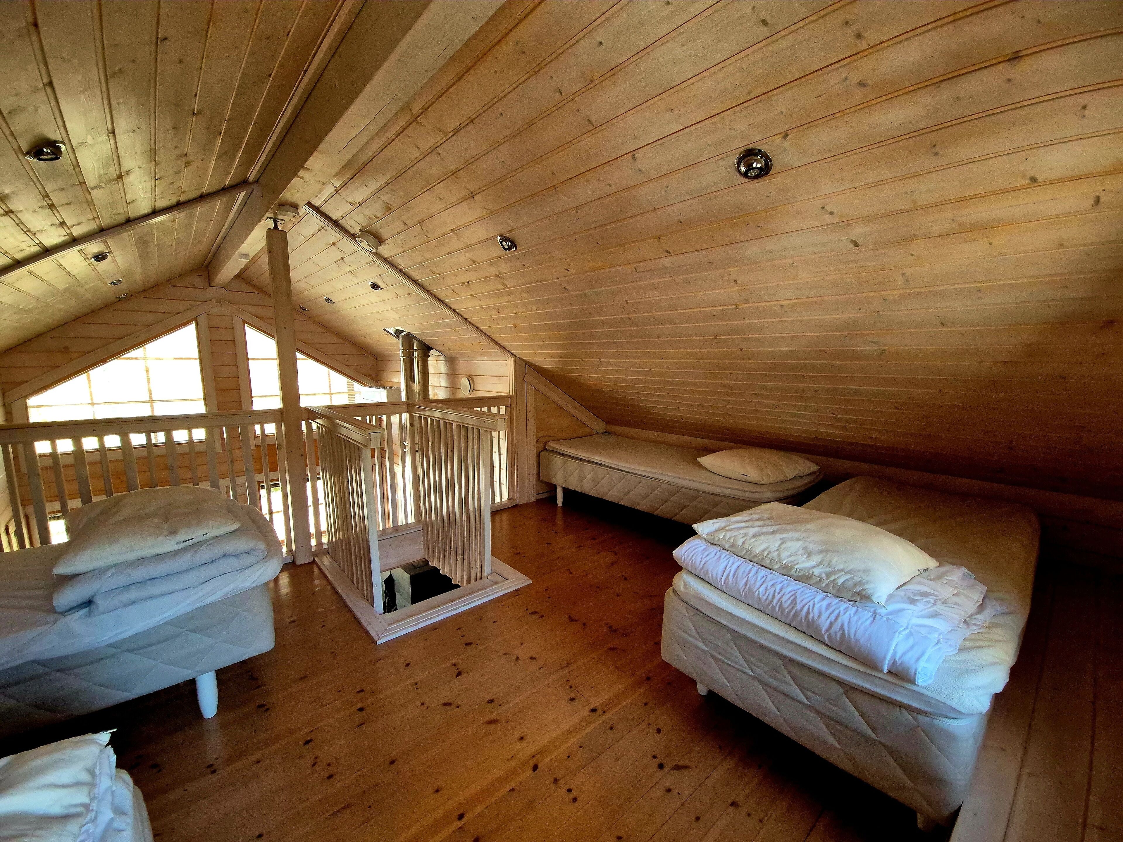 A cozy attic bedroom with wooden walls and sloped ceilings, featuring two beds and a small window.