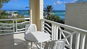 A balcony with white chairs and a table, overlooking the ocean and palm trees.
