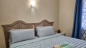 A neatly made bed with a patterned bedspread and two pillows, a nightstand with a lamp, and a wall-mounted light fixture.