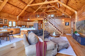 Ein geräumiger Innenraum einer Holzhütte mit einer Holztreppe, einer gemütlichen Sitzecke und einer Küche.
