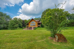 A log cabin with a stone foundation, a porch, and a large tree in front. - Waters Edge, Cozy Cabin & Pond (Creola)