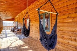 Eine Holzhütte mit zwei von der Decke hängenden Hängematten, einer Veranda mit Sitzgelegenheit und Blick auf den umliegenden Wald.