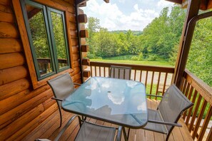 A wooden deck with a glass table and chairs, overlooking a green landscape.