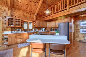 A wooden cabin interior with a kitchen area featuring a large island, two bar stools, and a refrigerator.