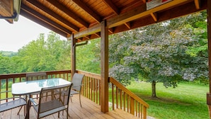 Um deck de madeira com mesa e cadeiras, com vista para uma área gramada e árvores.