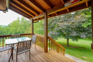 A wooden deck with a table and chairs, overlooking a grassy area and trees. - Waters Edge, Cozy Cabin & Pond (Creola)