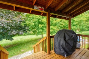 Terraza cubierta al aire libre con una parrilla y tanque de propano, rodeada por una barandilla de madera y un césped.