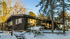 A wooden cabin with a covered porch, a small stream, and snow-covered ground.