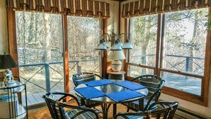 A sunroom with a table and chairs, large windows, and a hanging light fixture.