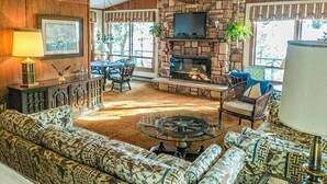 A living room with a stone fireplace, a television mounted above it, and a patterned sofa.