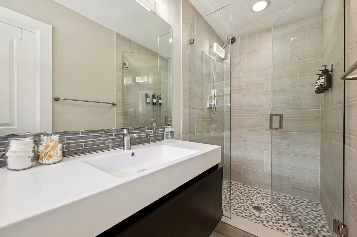 A modern bathroom with a glass-enclosed shower, a white sink, and a tiled backsplash.