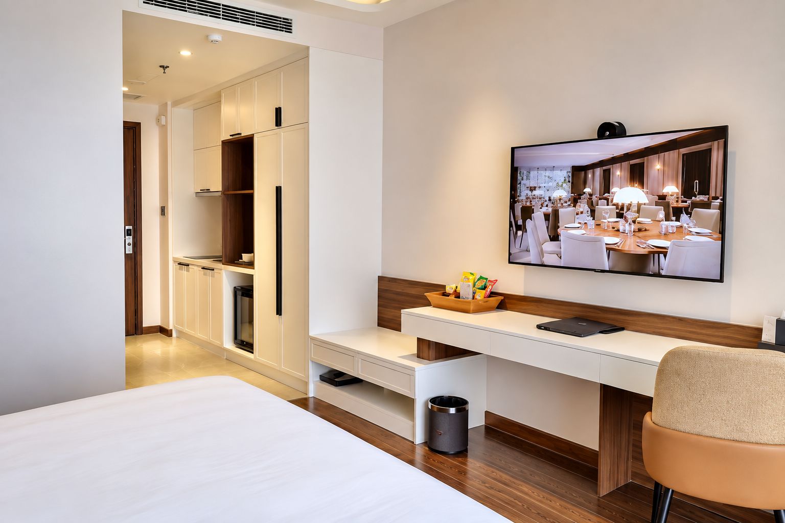 Een hotelkamer met een bed, een bureau met een laptop, een televisie en een kleine prullenbak.