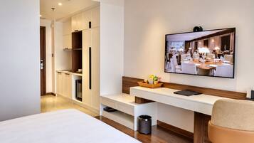 Een hotelkamer met een bed, een bureau met een laptop, een televisie en een kleine prullenbak.