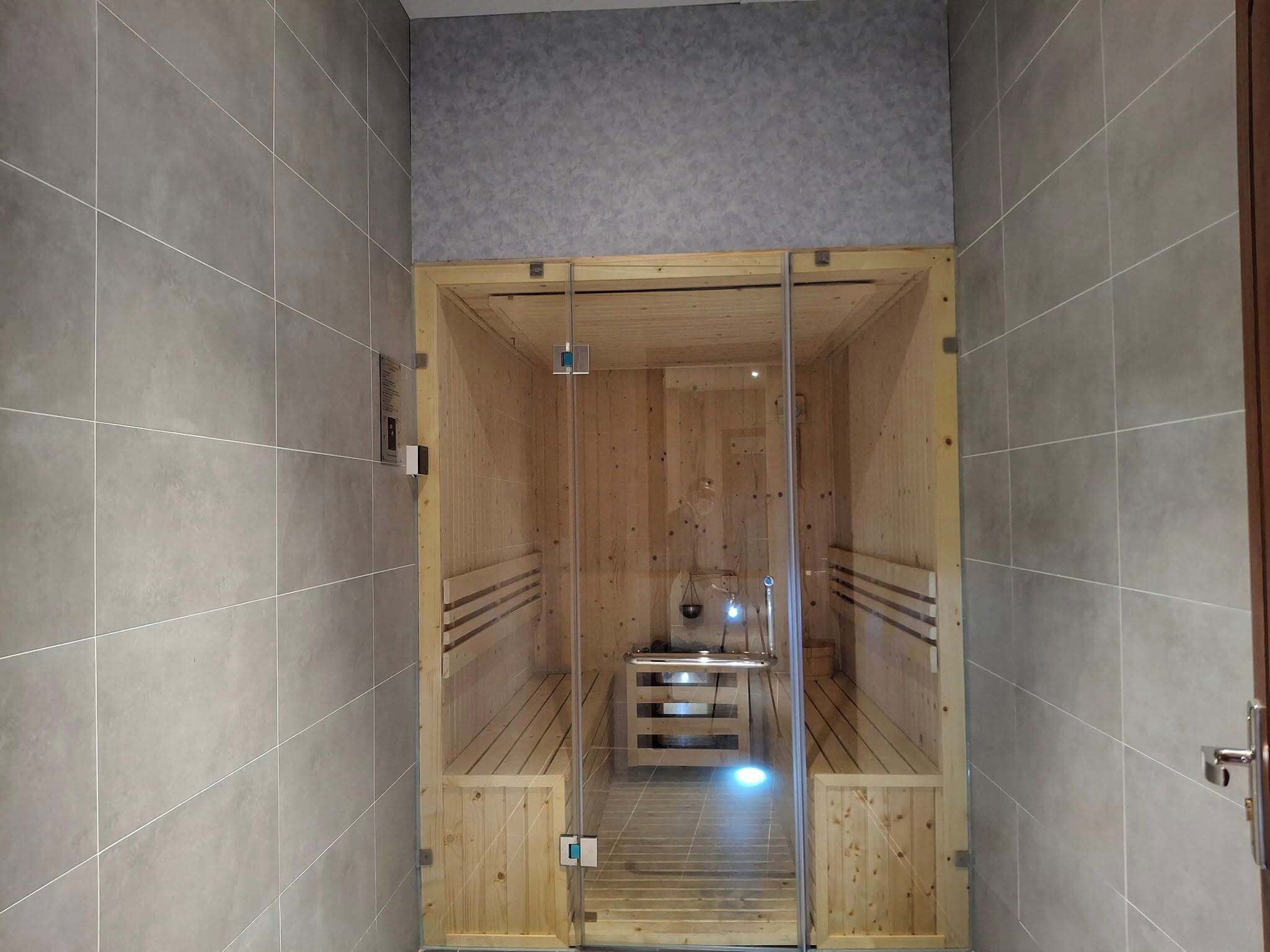 Una sauna con paredes de madera y puerta de vidrio, que incluye un banco y una mesita.