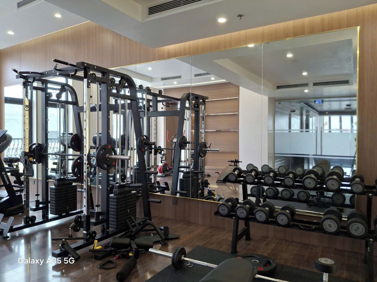 Un gimnasio con equipo de levantamiento de pesas, espejos y mancuernas.