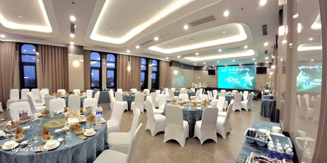 A conference room with round tables, white chairs, and a large screen displaying a presentation.