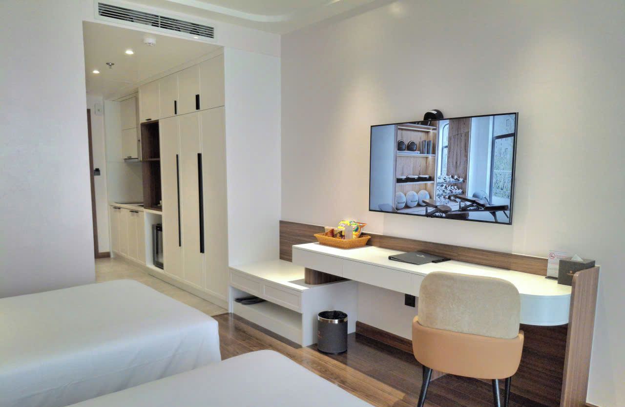 A hotel room with two beds, a desk, a chair, a TV, and a wardrobe.