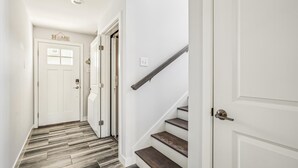 Ein Flur mit Holzboden, weißen Wänden und einer Treppe mit Holzstufen und einem Metallgeländer.