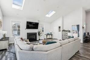 A spacious living room with a large sectional sofa, a fireplace, a flat-screen TV, and a skylight. - 5 Bedroom Bayside Beach House! (South Bethany)