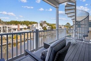 A covered outdoor deck with a spiral staircase, overlooking a body of water and residential buildings. - 5 Bedroom Bayside Beach House! (South Bethany)