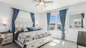 Ein Schlafzimmer mit Bett, Nachttischen, einem Schminktisch, einem Deckenventilator und einem Fenster mit Vorhängen.