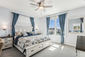A bedroom with a bed, nightstands, a dresser, a ceiling fan, and a window with curtains.