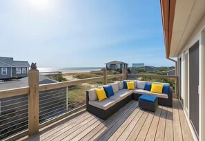 A wooden deck with a sectional sofa and a small table, overlooking a beach and other buildings. - Gatsby’s Sky Level. Ocean Bay Park. 
Sleeps 12. Hot Tub + Ocean Views (Fire Island)