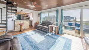A spacious living area with a large window, a ceiling fan, and a fireplace. - Gatsby’s Sky Level. Ocean Bay Park. 
Sleeps 12. Hot Tub + Ocean Views (Fire Island)