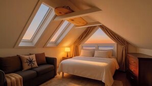 A bedroom with a sloped ceiling, skylights, a bed, a sofa, a nightstand, and a dresser. - Gatsby’s Sky Level. Ocean Bay Park. 
Sleeps 12. Hot Tub + Ocean Views (Fire Island)