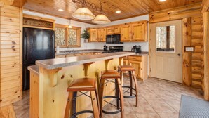 A log cabin kitchen with a central island, wooden cabinets, and a black refrigerator. - Fawn Lake Retreat | Pontoon, Beach & Game Room (Crosslake)