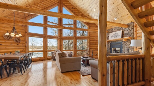 A spacious log cabin interior with a dining area, sofas, and a stone fireplace. - Fawn Lake Retreat | Pontoon, Beach & Game Room (Crosslake)
