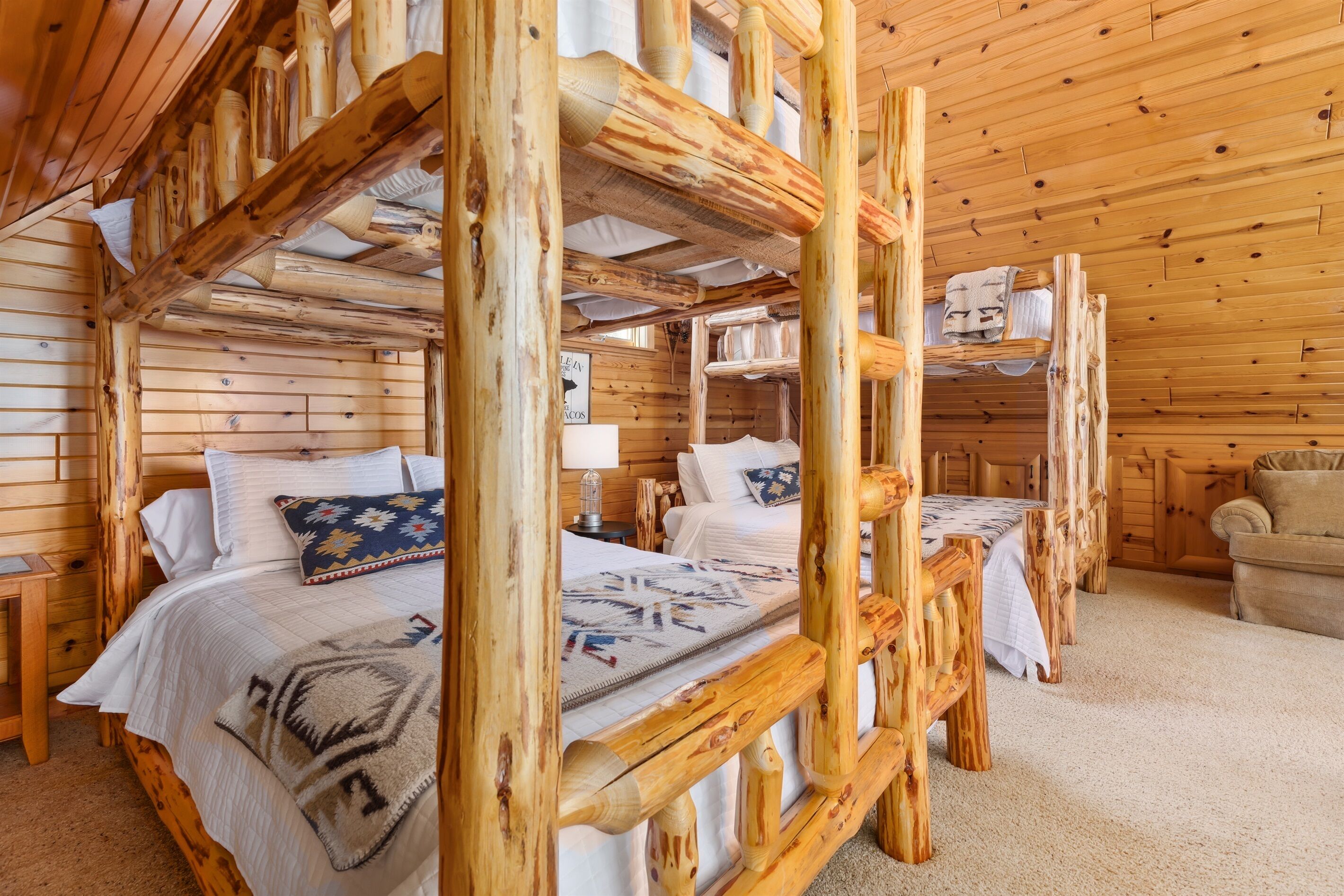 Interior de una cabaña de madera con literas, un sofá y una mesita.