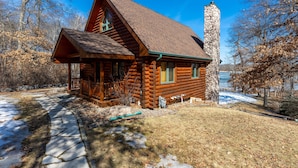 A log cabin with a stone chimney, a porch, and a stone pathway leading to the entrance. - Fawn Lake Retreat | Pontoon, Beach & Game Room (Crosslake)