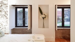 A bedroom with a bed, two windows, a vase with flowers, and a towel on the bed. - Great Flat & View in Historic Porto by LovelyStay (Porto)