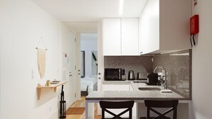 A compact kitchen with white cabinets, a granite countertop, a microwave, a coffee maker, and a sink. There are two chairs at the counter. - Great Flat & View in Historic Porto by LovelyStay (Porto)