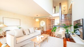 A modern living room with a sofa, coffee table, and chairs. There is a staircase leading to an upper level.