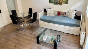 Una sala de estar moderna con una mesa de centro de vidrio, un sofá con cojines estampados y una zona de comedor con una mesa de vidrio y sillas negras.
