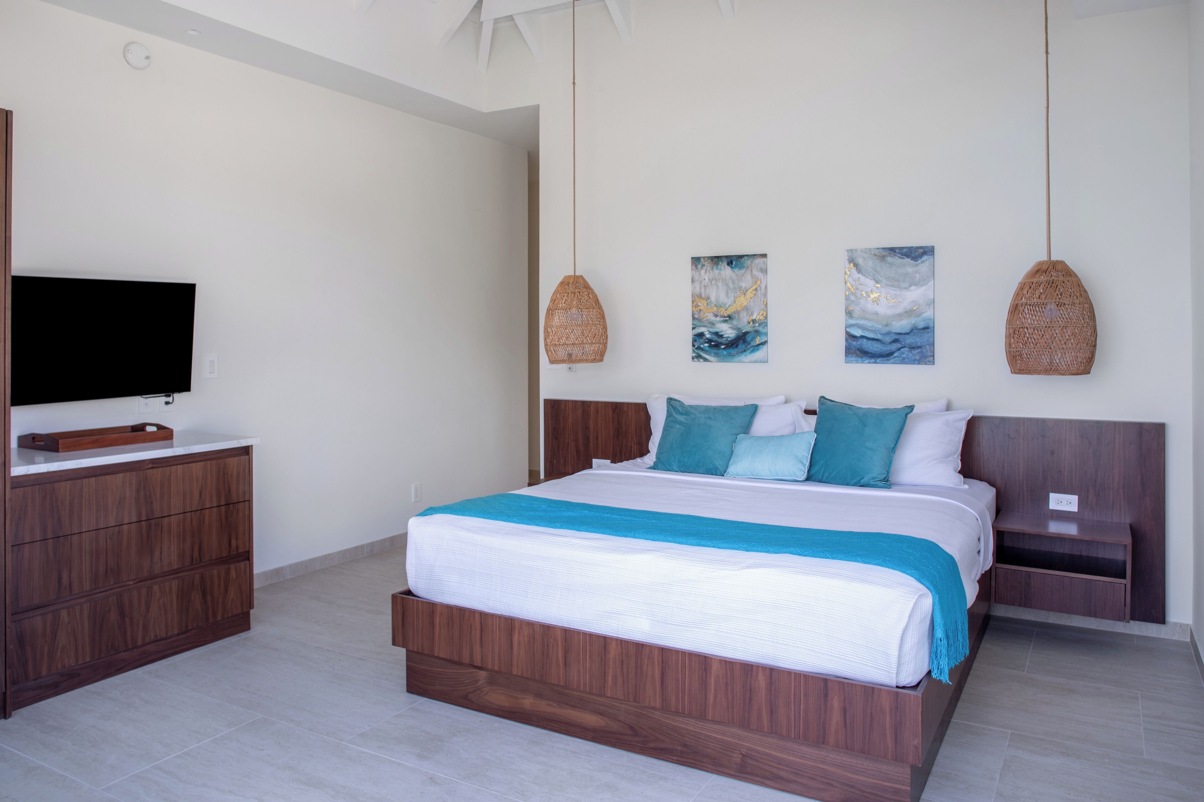 A modern bedroom with a large bed, wooden nightstands, a flat-screen TV, and two wall-mounted artworks.