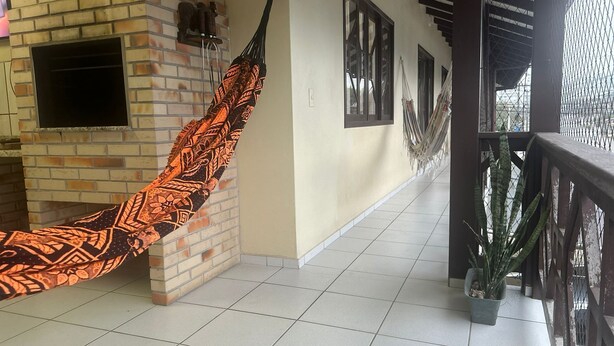 Un piso de baldosas, una pared de ladrillo, una hamaca, una planta en maceta y una ventana.