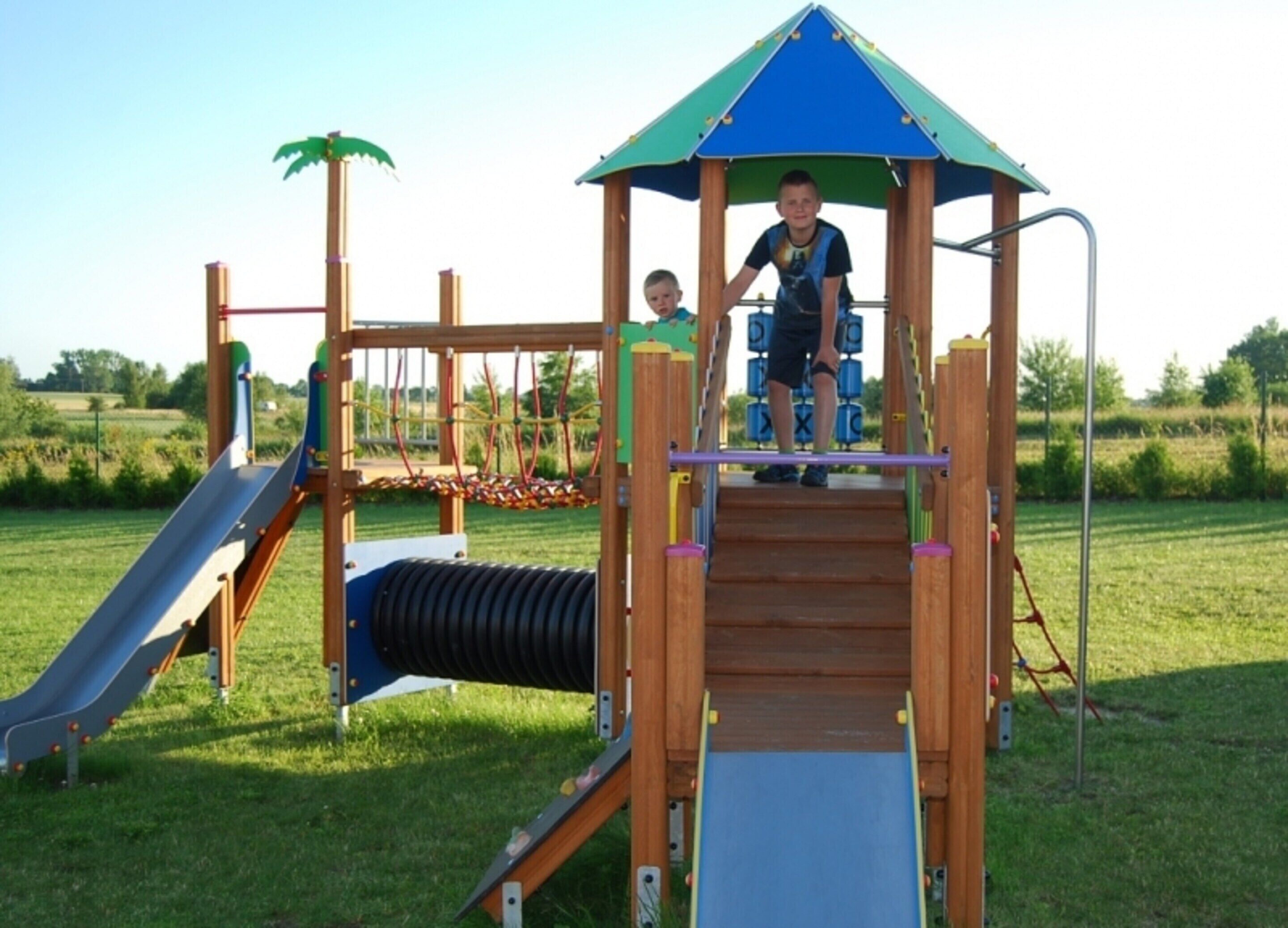 A playground with a slide, climbing net, and a wooden playhouse with a blue roof.
